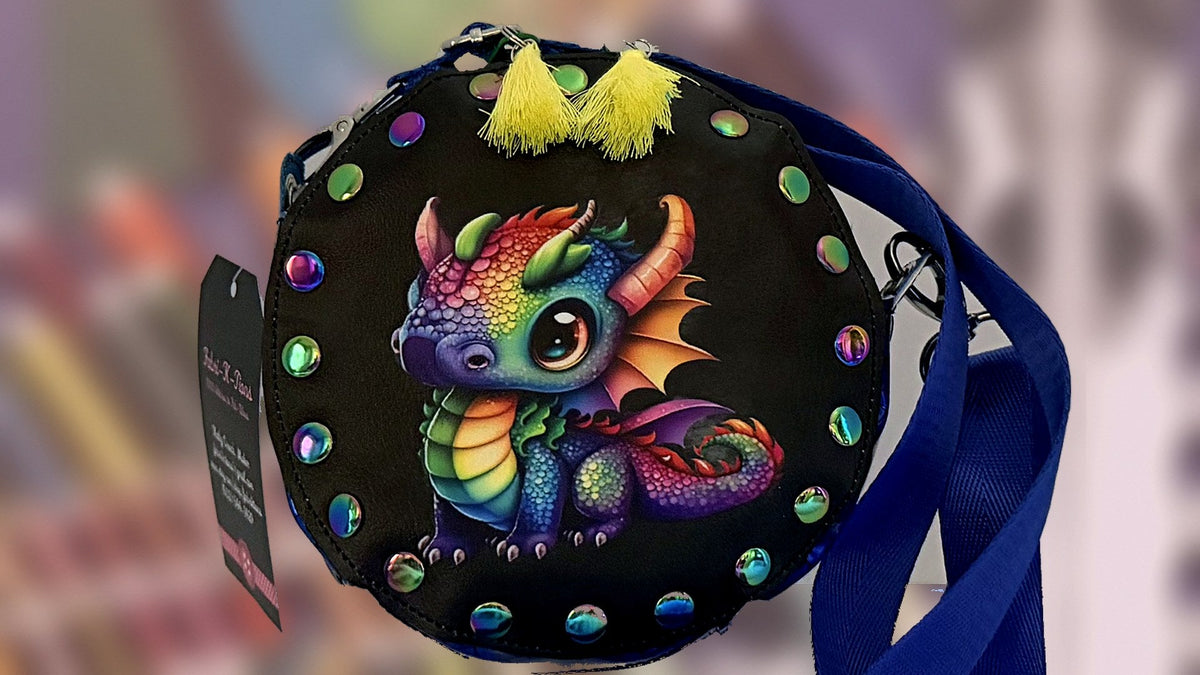 Round rivet crossbody bag with a rainbow baby dragon panel and blue strap, handmade in Louisville, KY