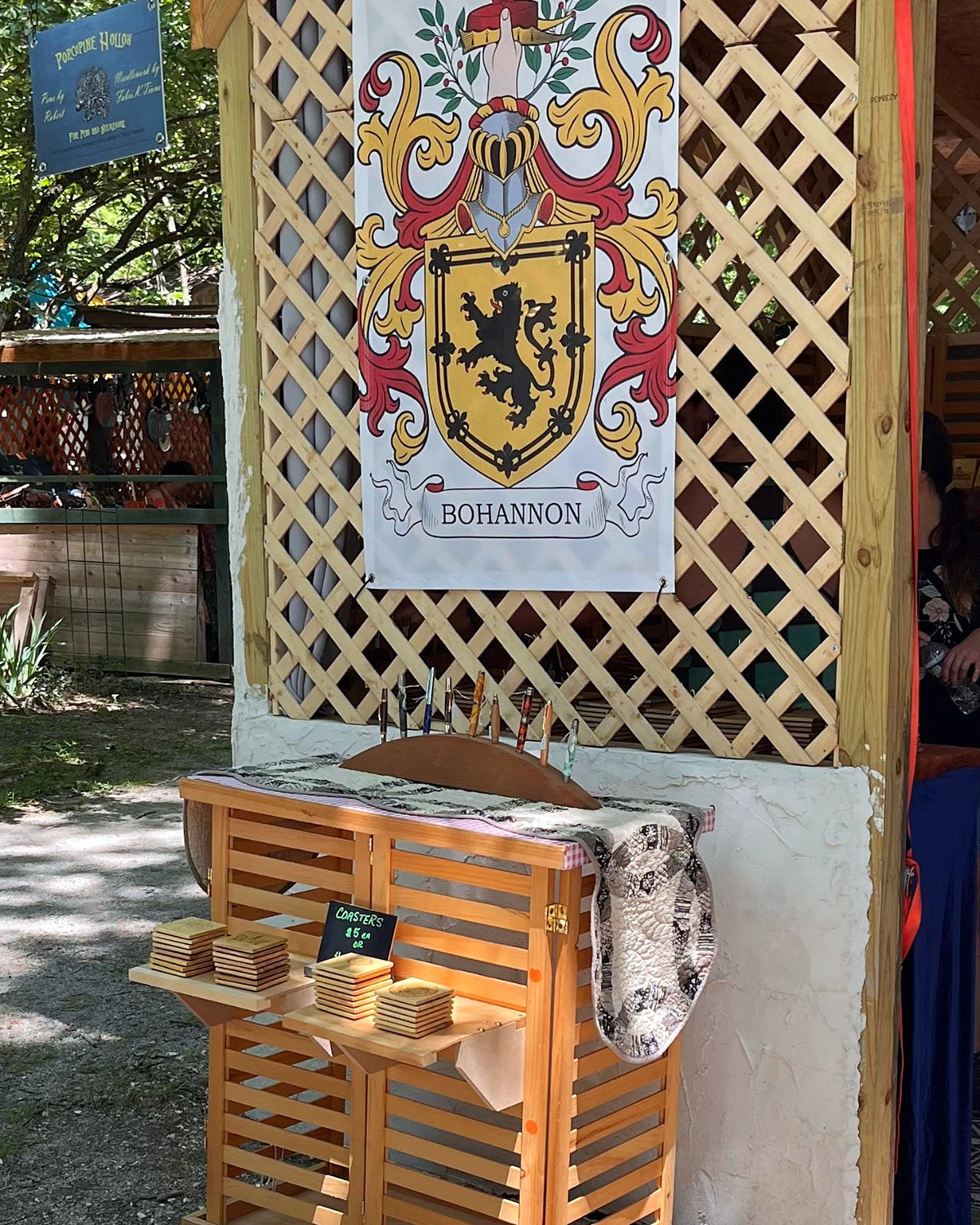 Lattice wall with a family crest banner and a wooden display at a Fabri-K-Tions festival booth