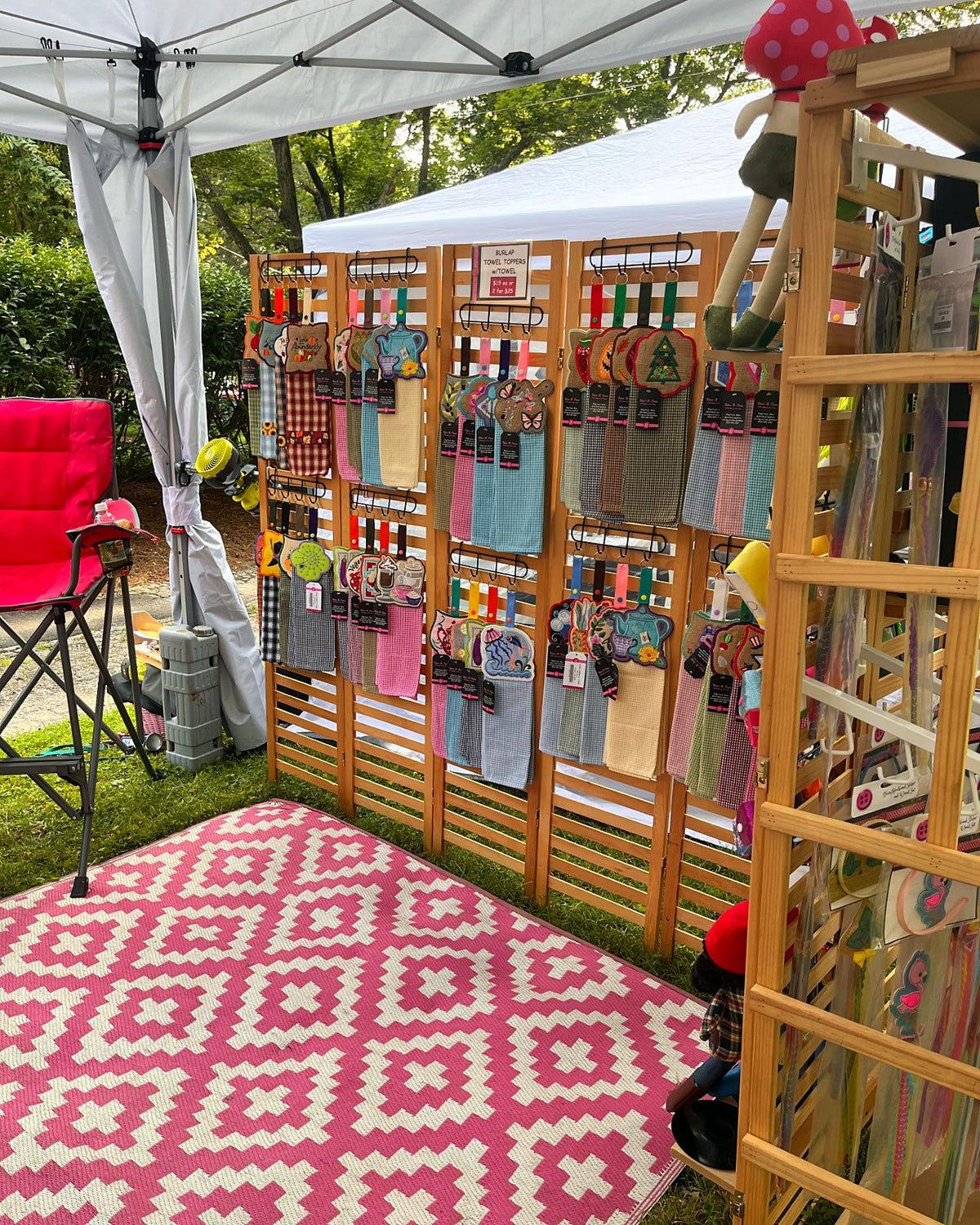 Fabri-K-Tions outdoor booth with wooden shelves of handmade pieces and a pink patterned rug