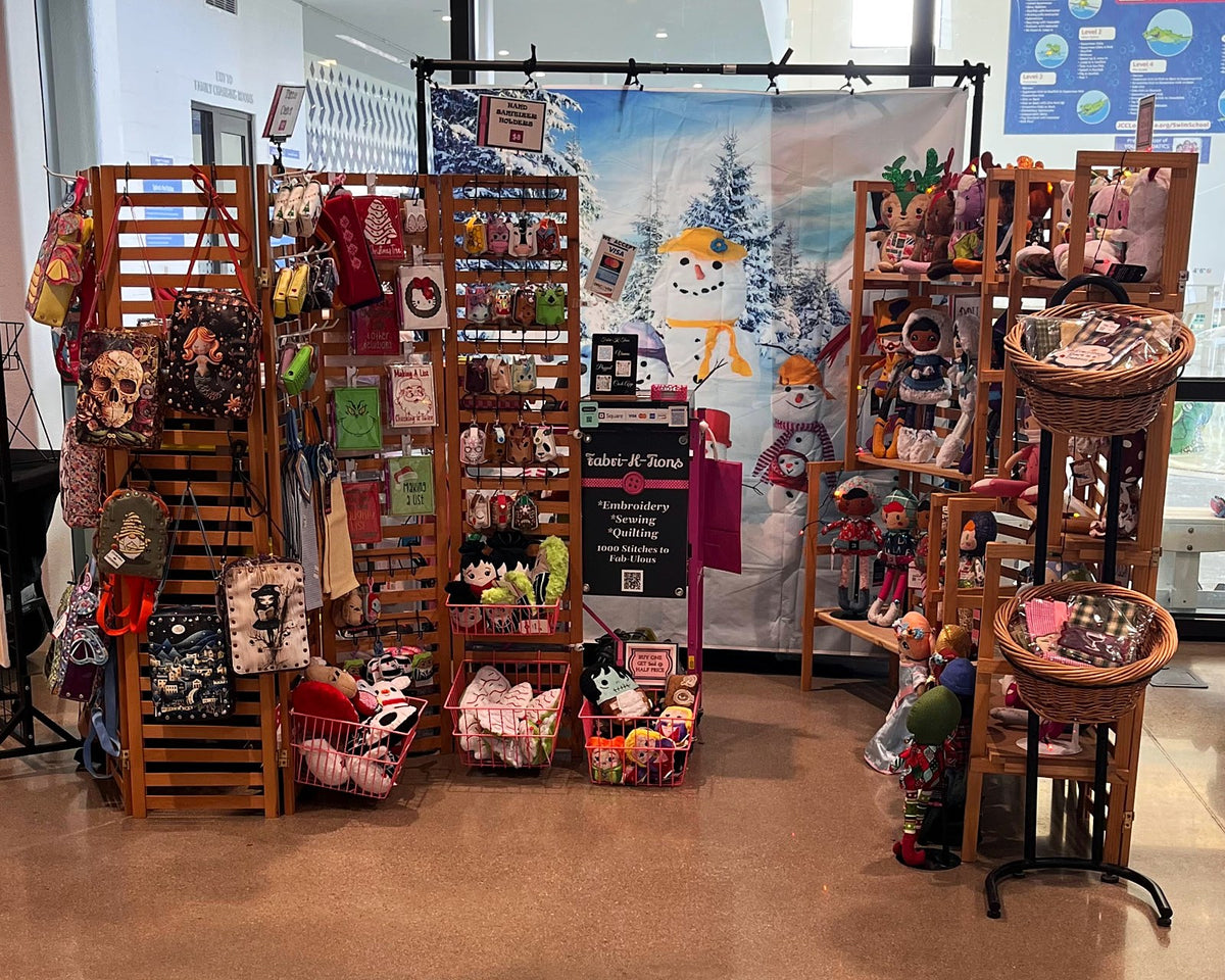 Fabri-K-Tions indoor craft market booth with wooden racks of handmade gifts