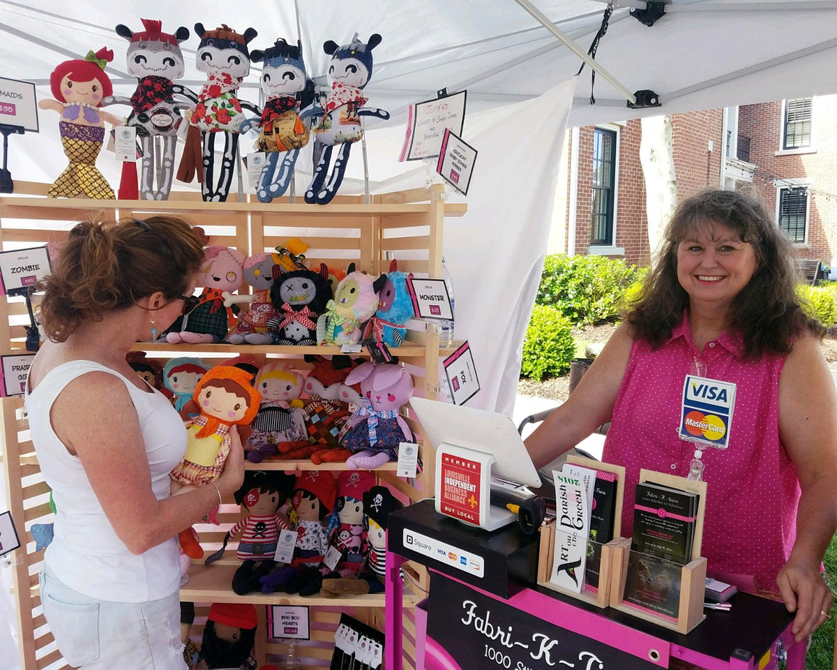 Kathy Creech of Fabri-K-Tions helping a customer at her festival booth full of handmade cloth dolls