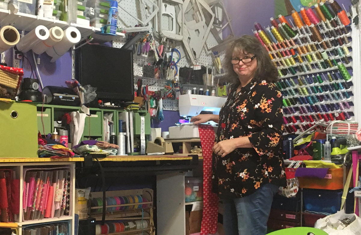 Kathy Creech of Fabri-K-Tions at her sewing machine in her Louisville, KY studio, with a wall of embroidery thread behind her